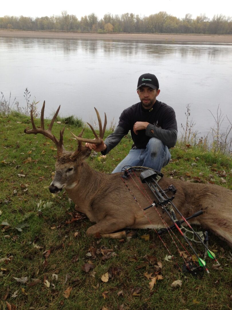 A man with a hunting bow posing with a dead deer