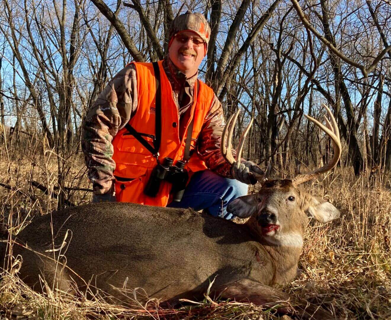 A man in an orange vest holding a dead deer by the antlers