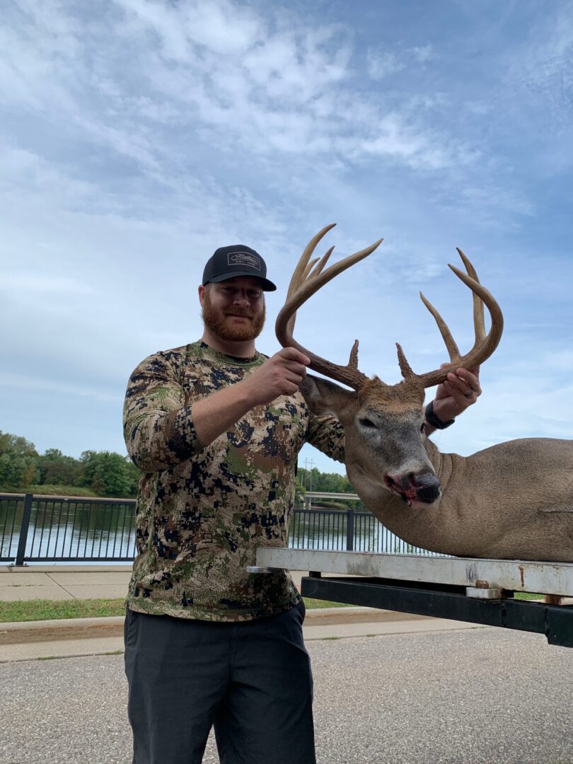 A man in a camouflage sweater olding a dead deer by the antlers