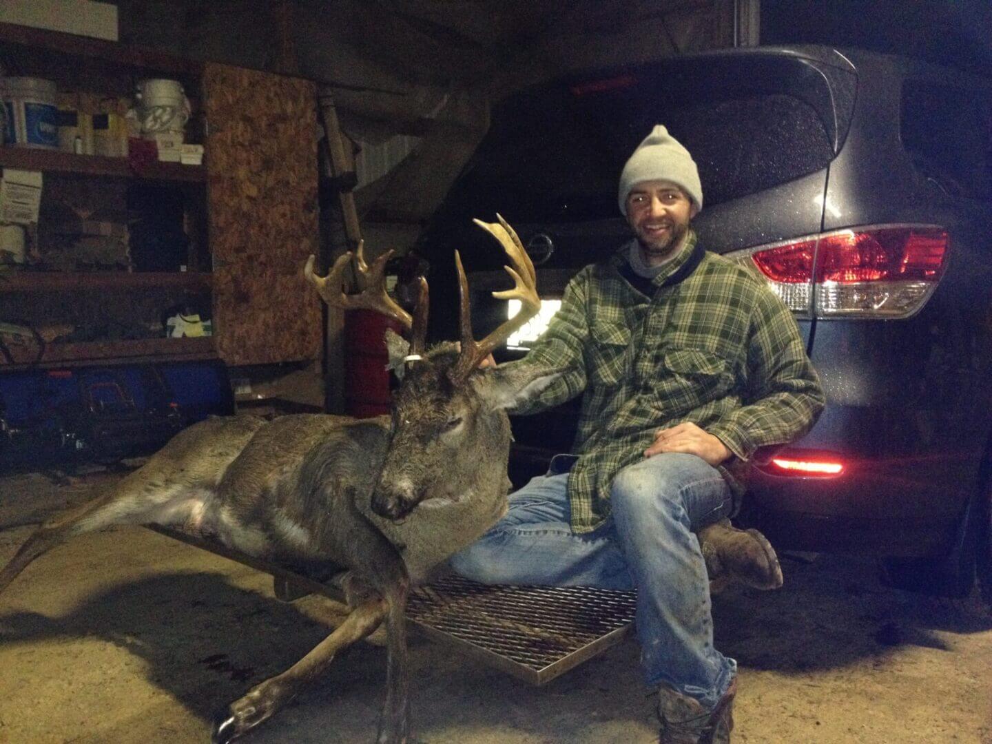 A man posing with a dead deer on the back of an SUV