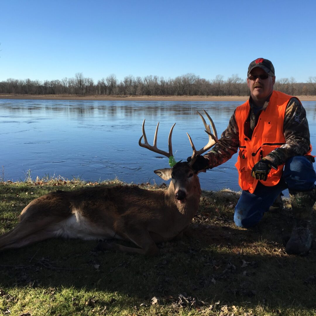 A hunter holding a deer by the antlers beside a lake