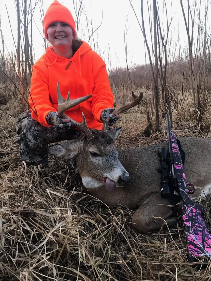A woman in an orange hoodie posing with a dead deer