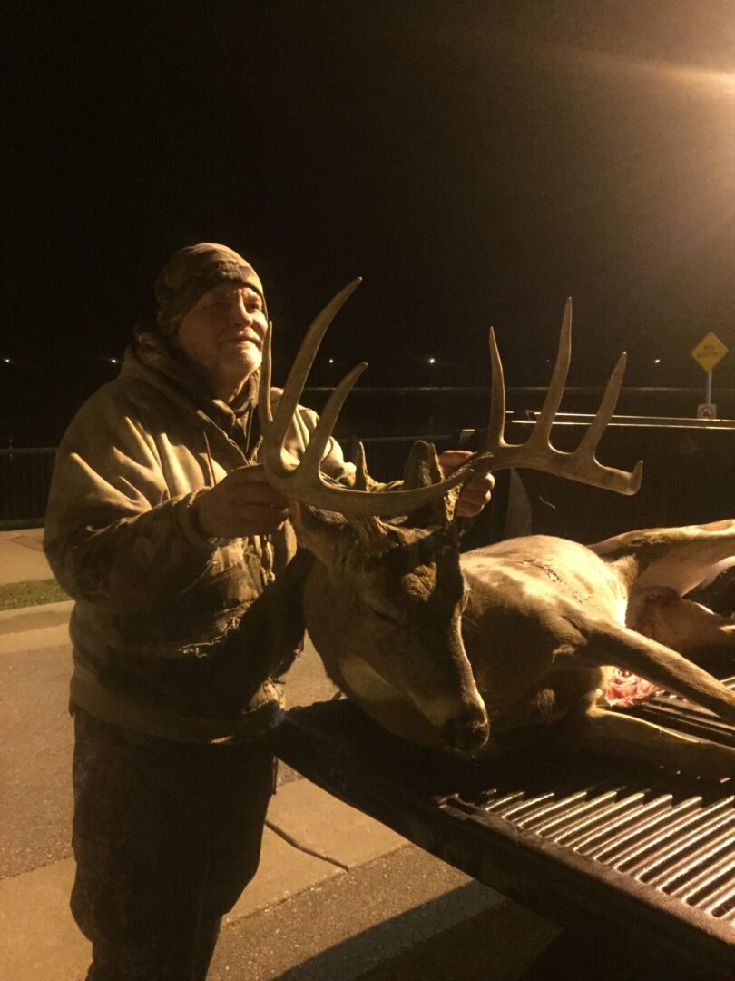 An old man grabbing a dead deer by the antlers