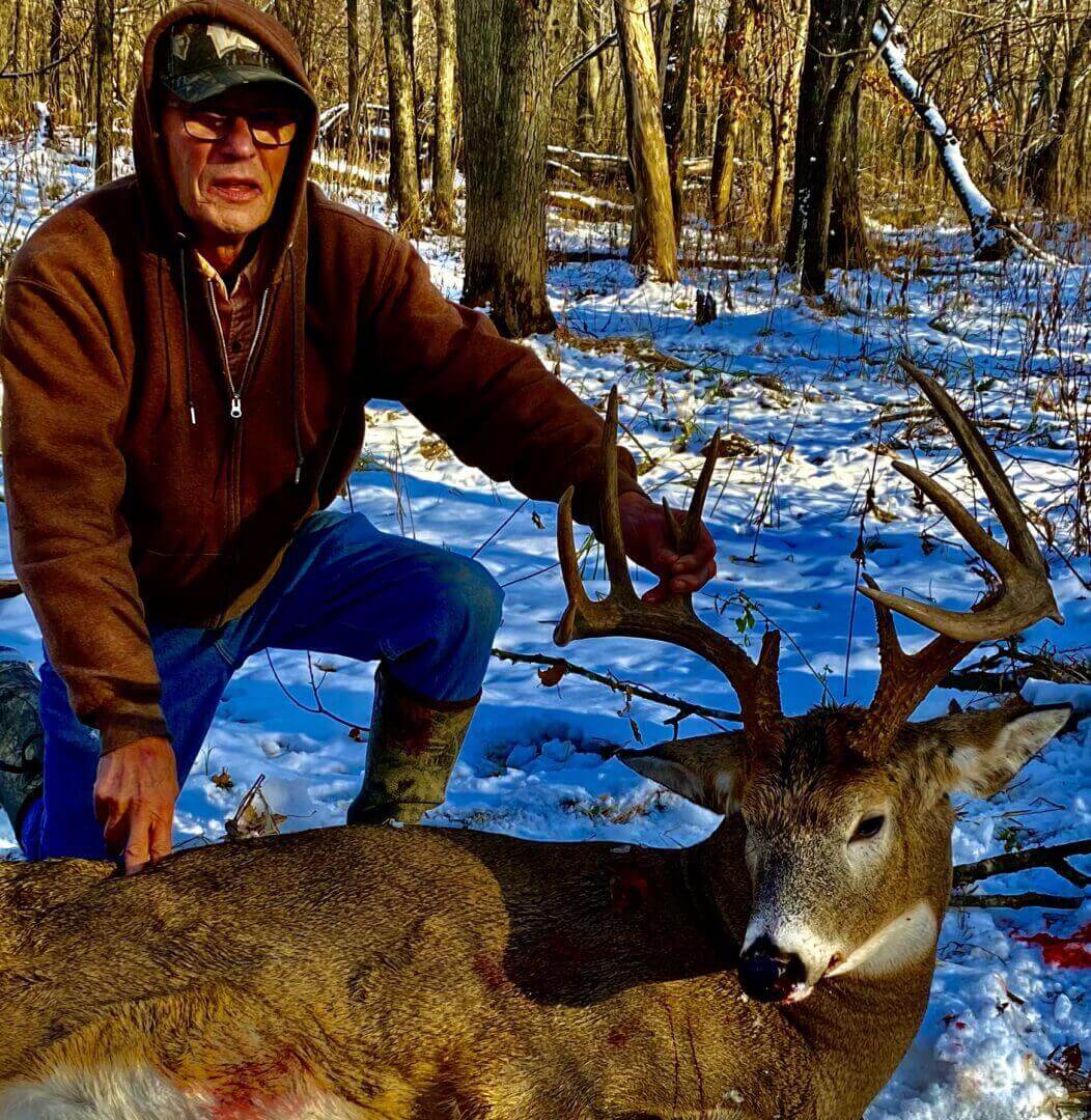 A man in a brown hoodie grabbing a dead deer by the antlers