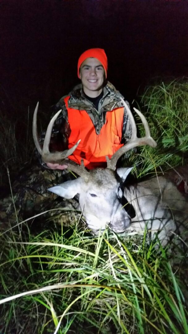 A man in a camouflage hoodie with a dead deer