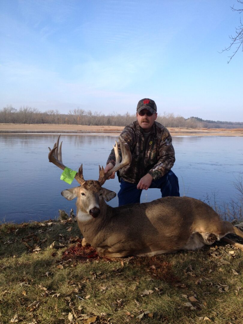 A man in sunglasses holding a dead deer by the antlers