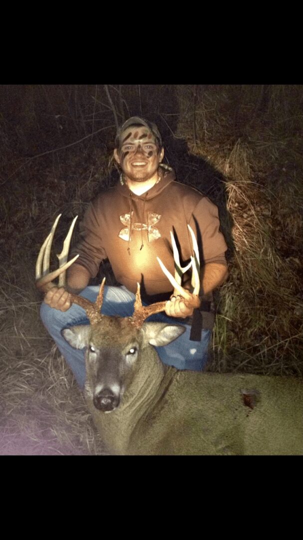 A man with face paint holding a dead deer by the antlers