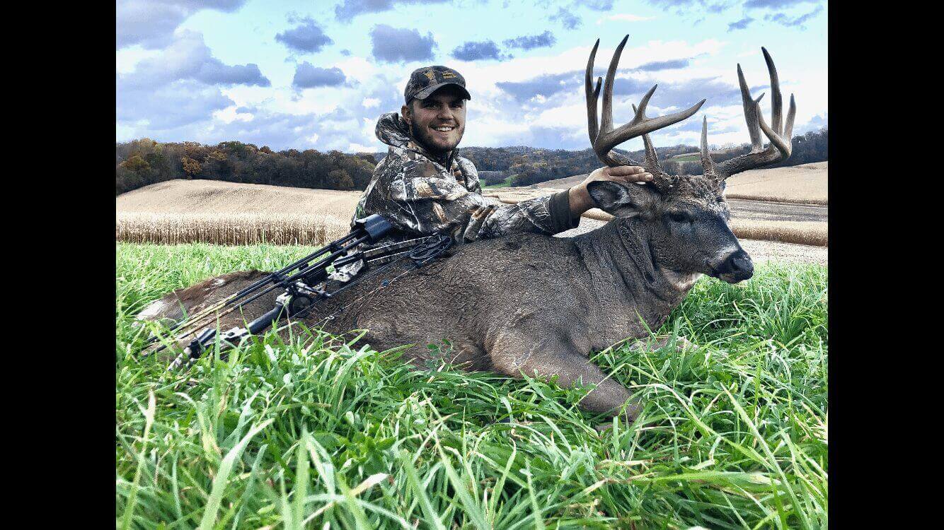 A man in a camouflage hoodie with a dead deer
