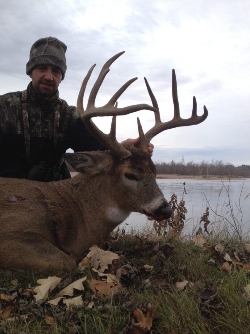 A man in a camouflage hoodie with a dead deer