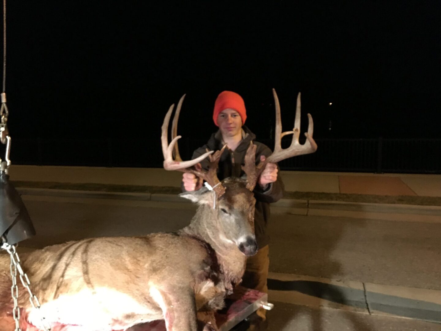A young man with an orange bonnet posing with a dead deer